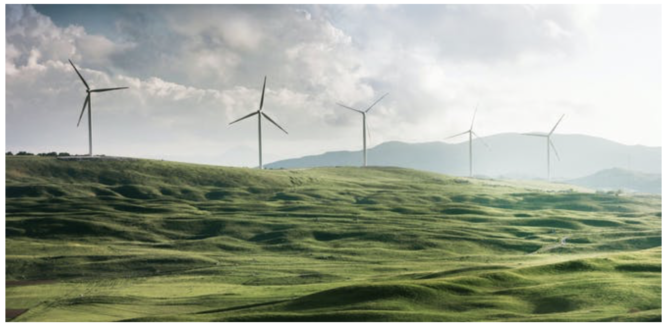 Five windmills on a green hill with a cloudy blue sky in the background.